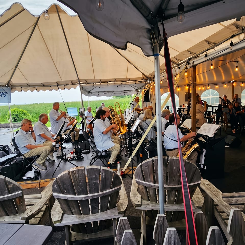 Live swing band performs under a tent beside an outdoor dining area filled with wooden chairs and guests.