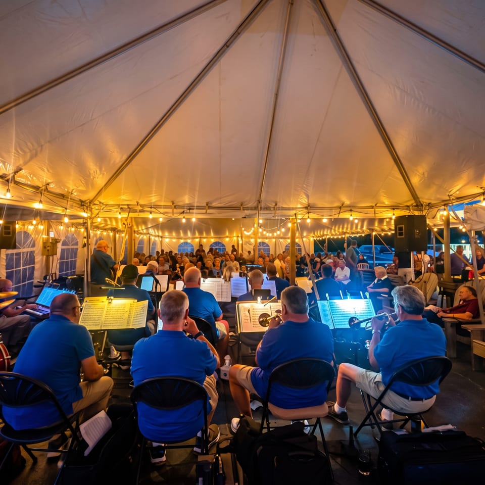 Musicians perform for a seated audience inside a warmly lit outdoor event tent decorated with string lights.